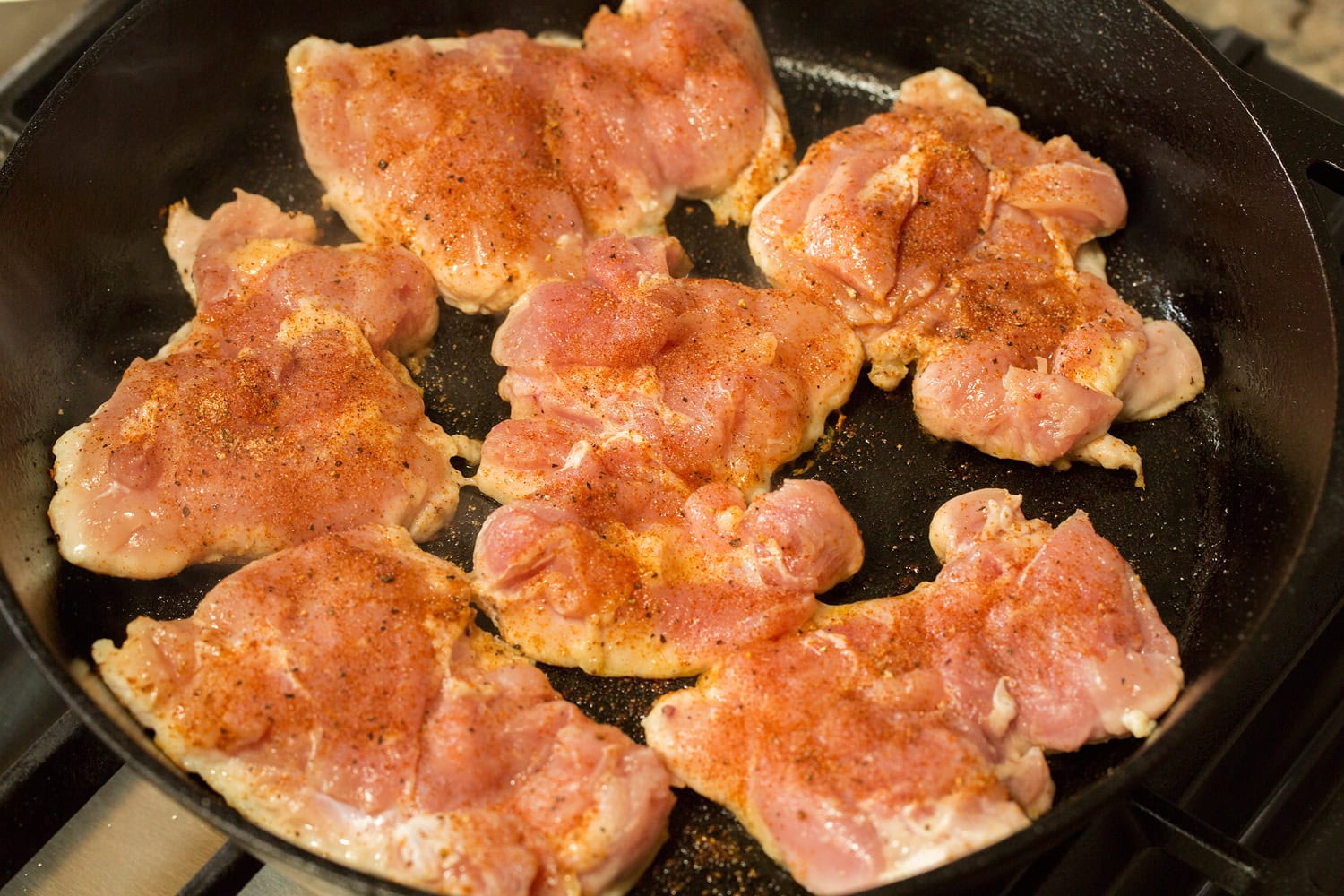 Raw chicken thighs searing in a cast iron pan.
