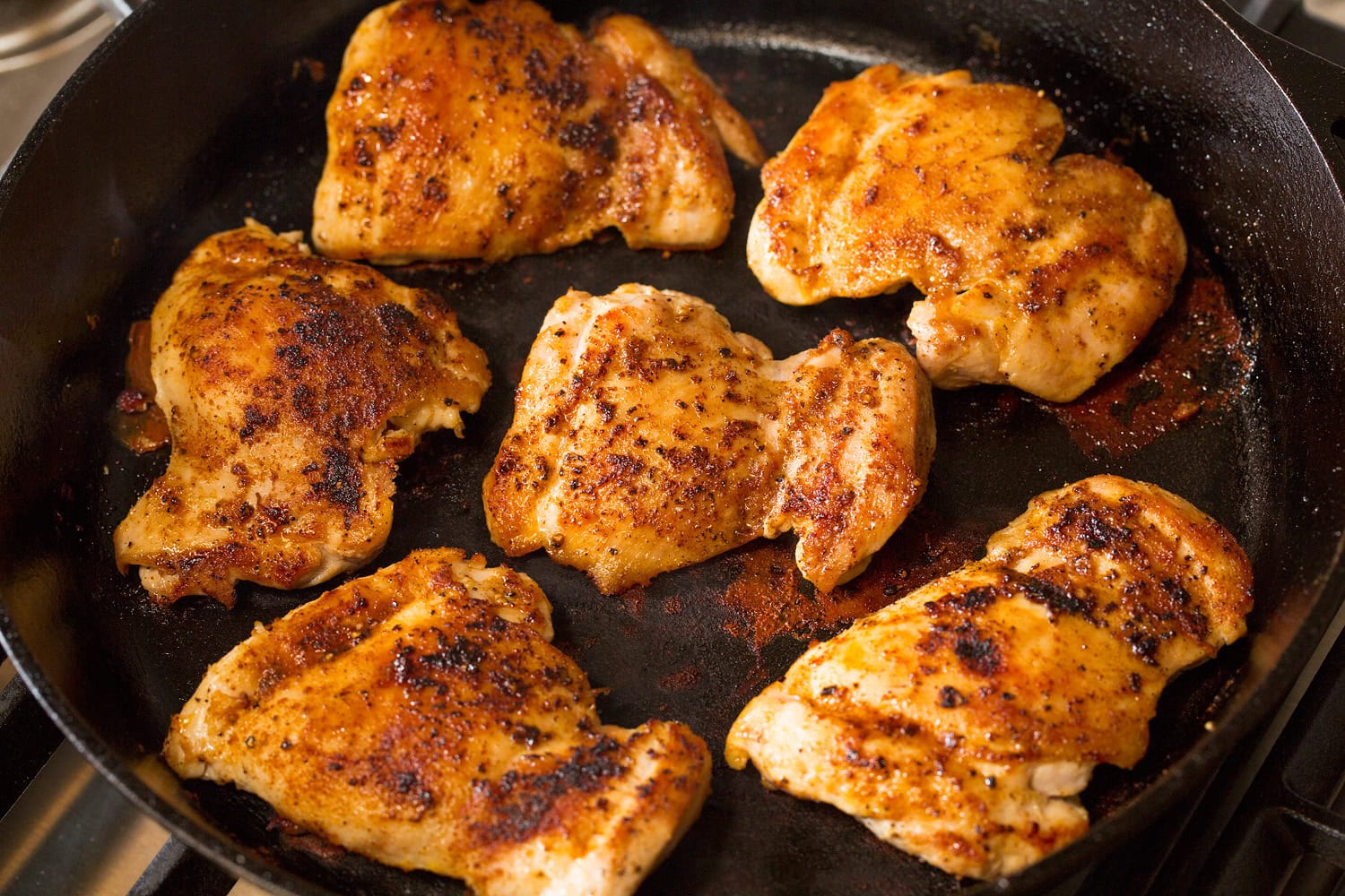 Chicken thighs shown cooked through in a cast iron pan on second side.