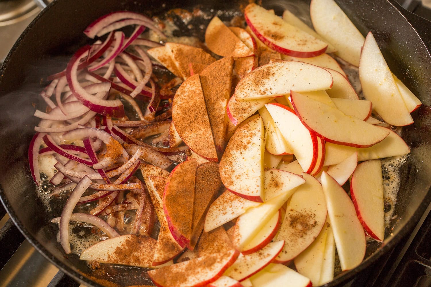 Apples spices and red onions added to skillet.