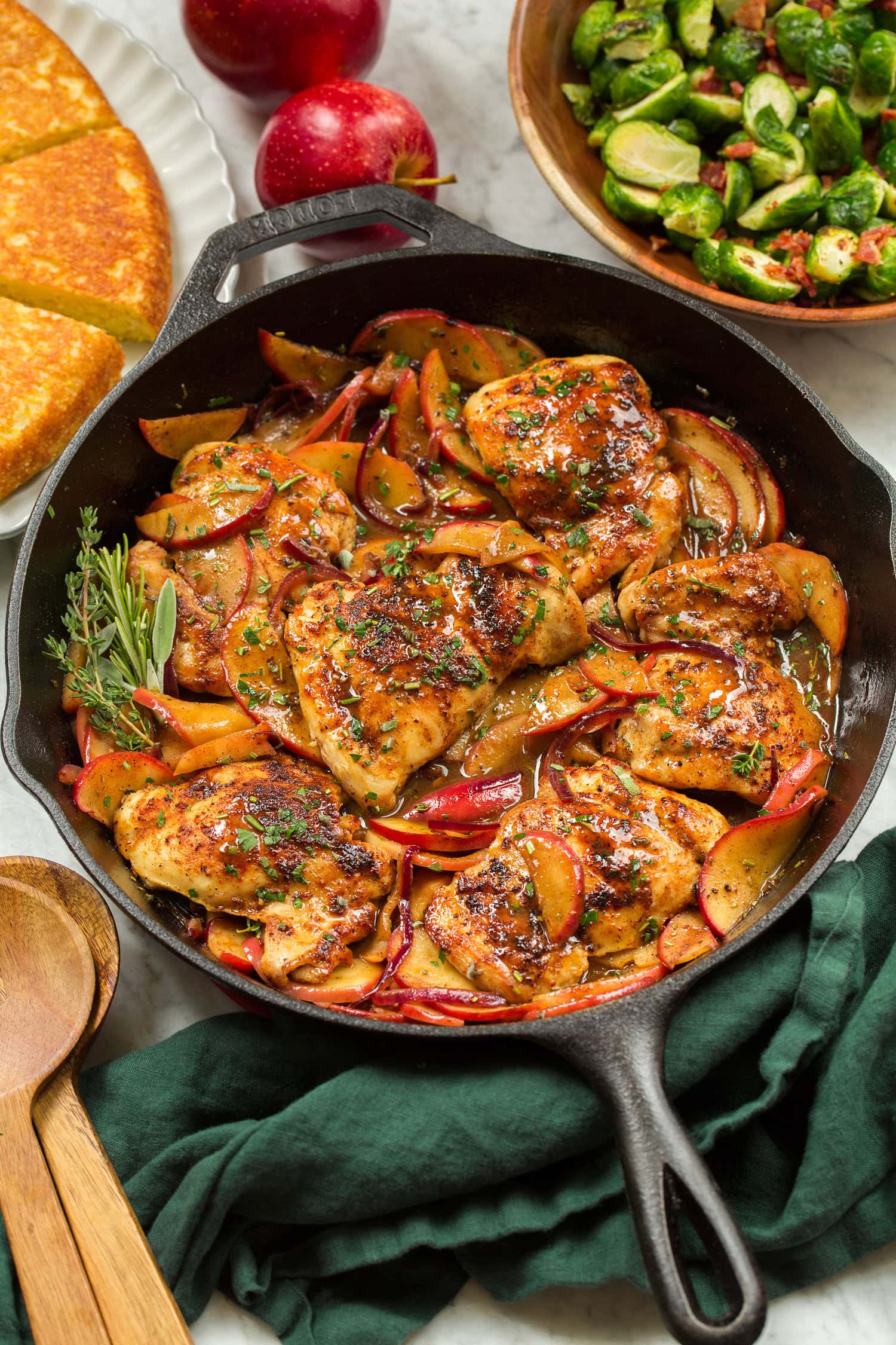 Chicken and apples layered together in cast iron skillet with herb garnish.