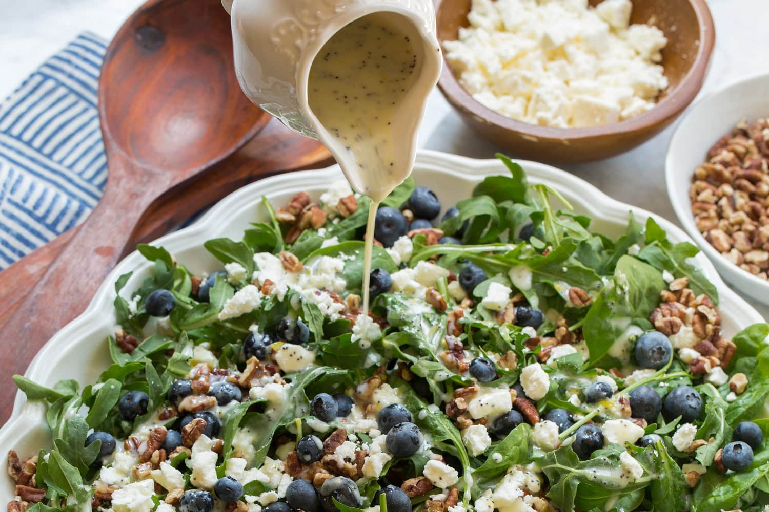 Lemon poppy seed dressing being drizzled over blueberry arugula salad.
