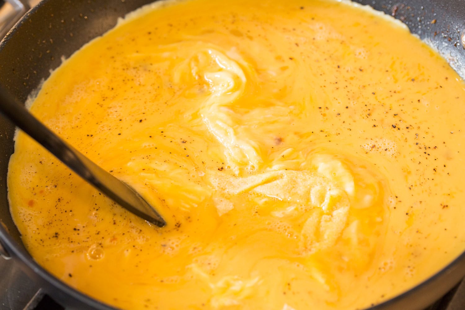 Breakfast Bowls Stirring scrambled eggs in a non-stick skillet with a spatula.
