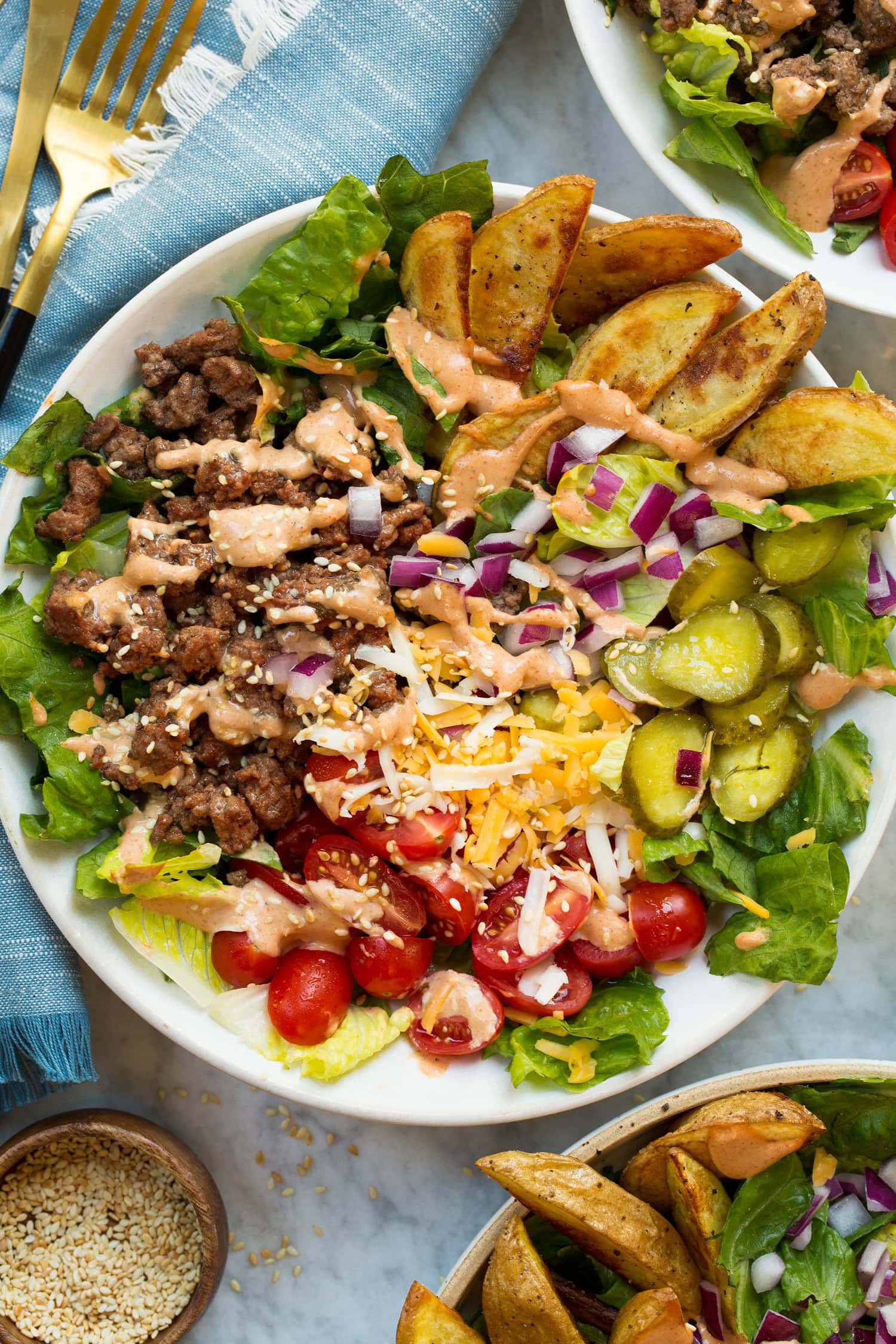 Single serving burger bowl showing ground beef, pickles, tomatoes, cheese, onion, baked fries and lettuce.