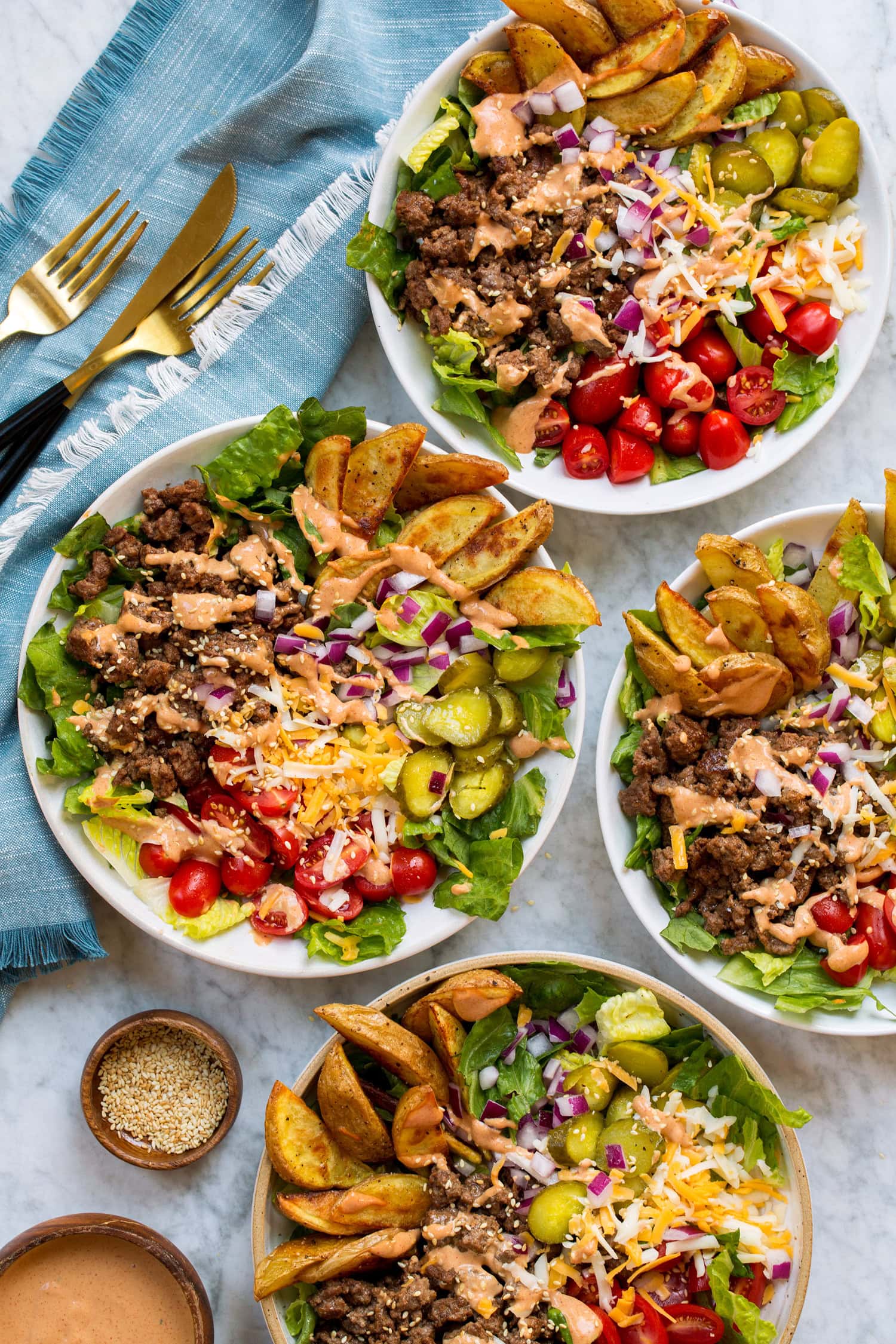 Four burger bowls shown from overhead on a marble surface with a blue cloth to the side.