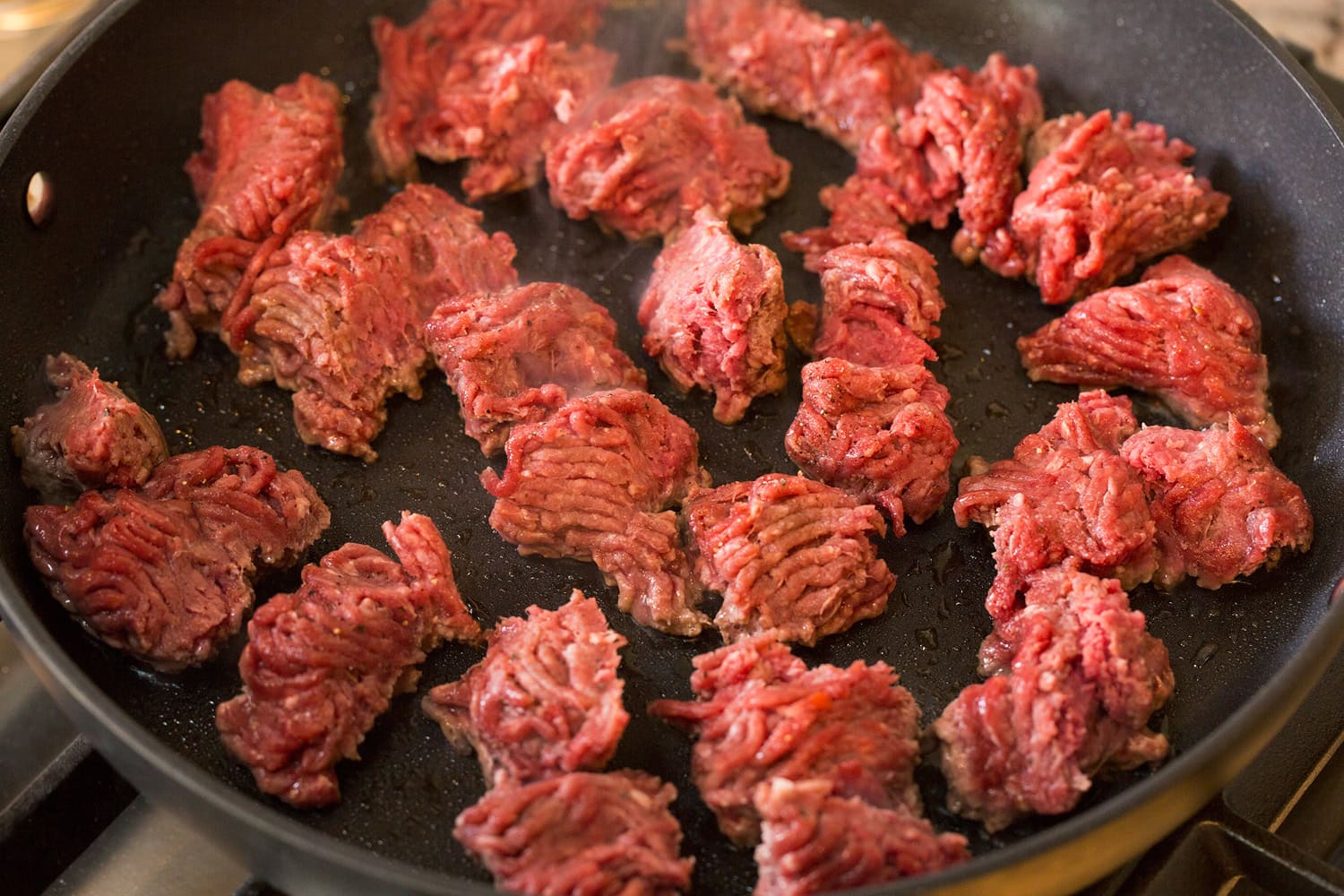 Raw ground beef in skillet in chunks.