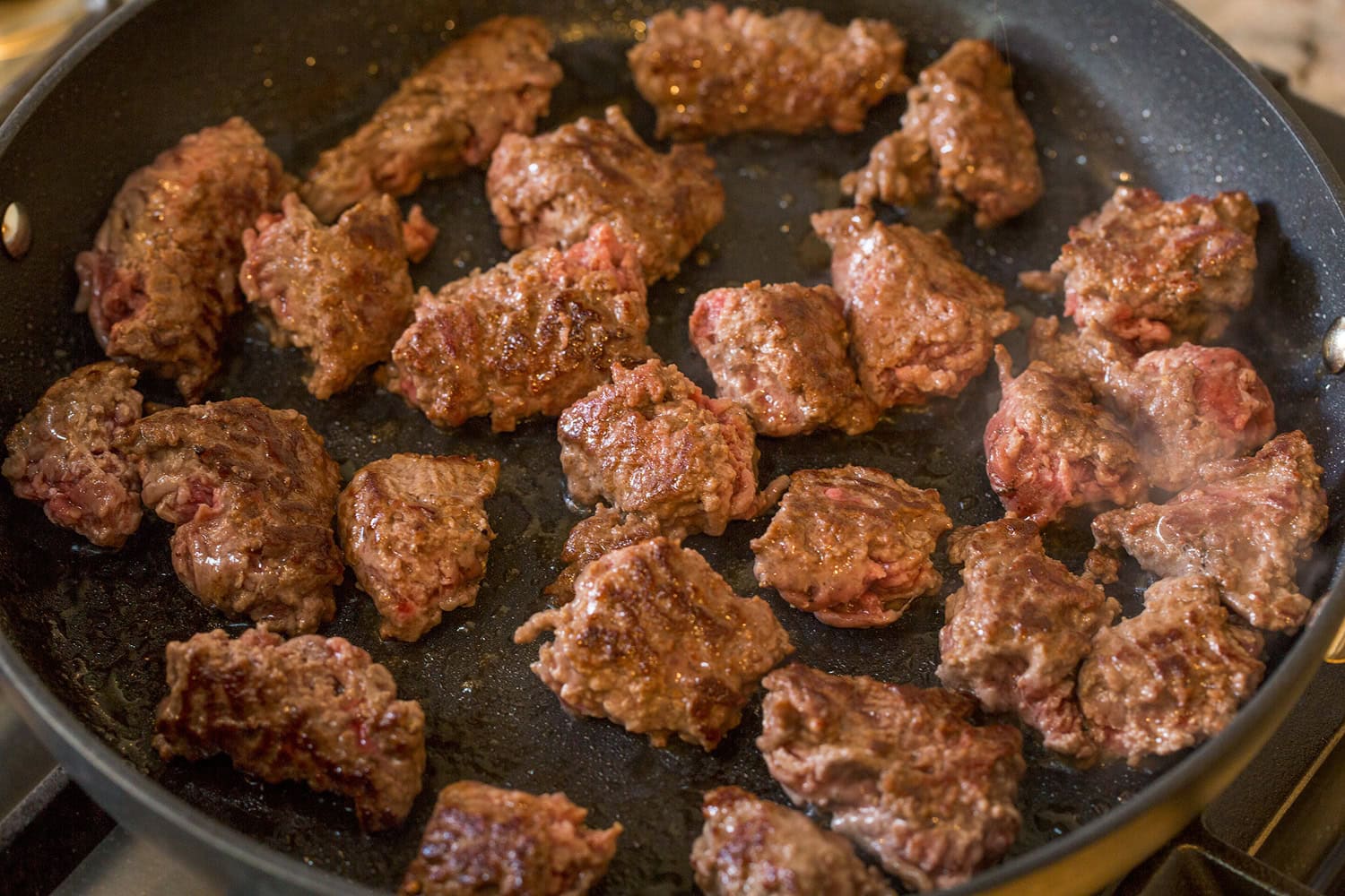 Beef chunks in skillet turned to show golden brown side.