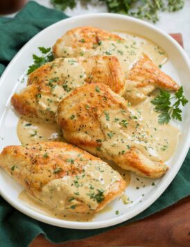 Creamy dijon mustard chicken shown on a white oval serving platter over a green cloth and a wooden tray.