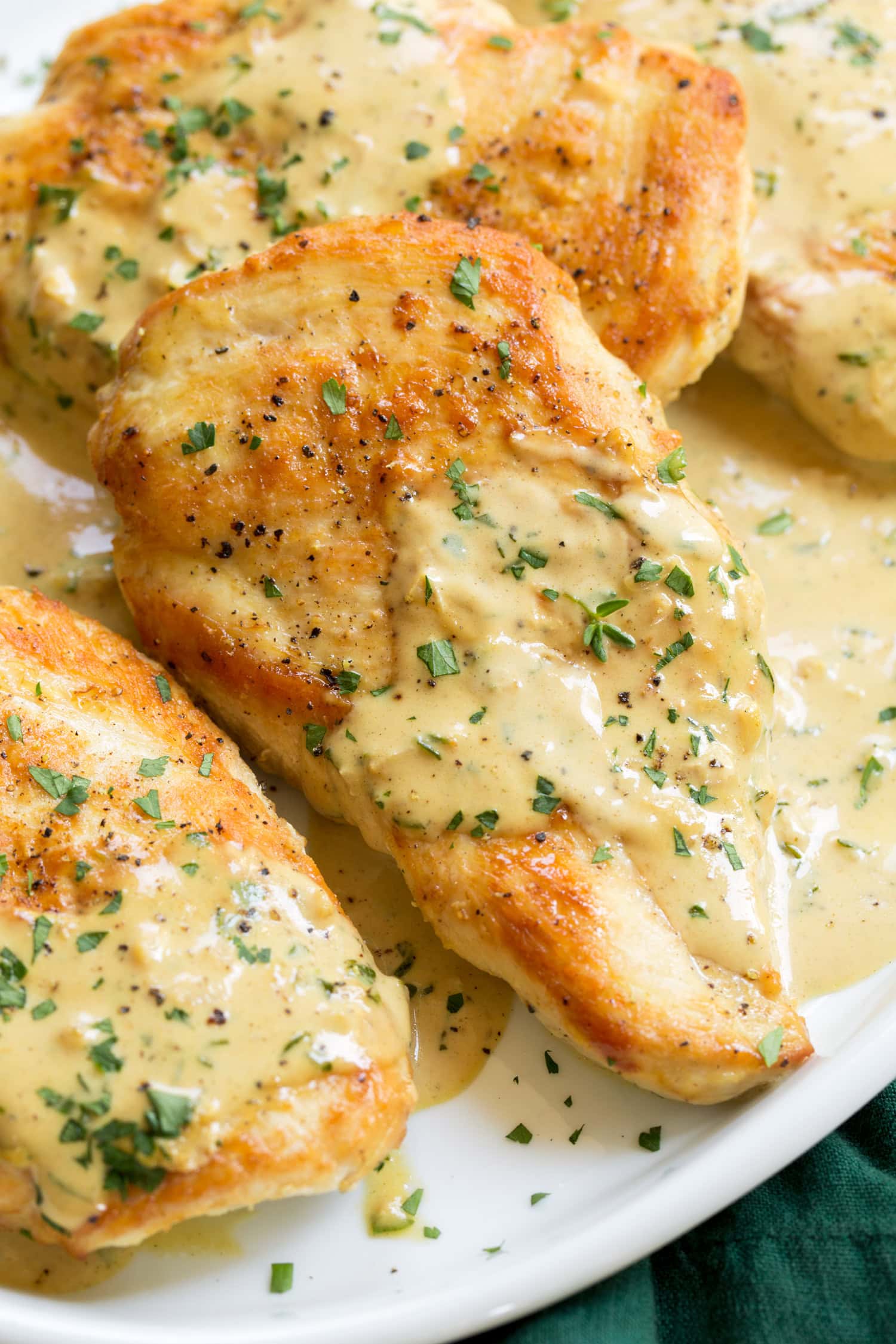 Golden brown chicken breast with mustard sauce and herbs shown close up.