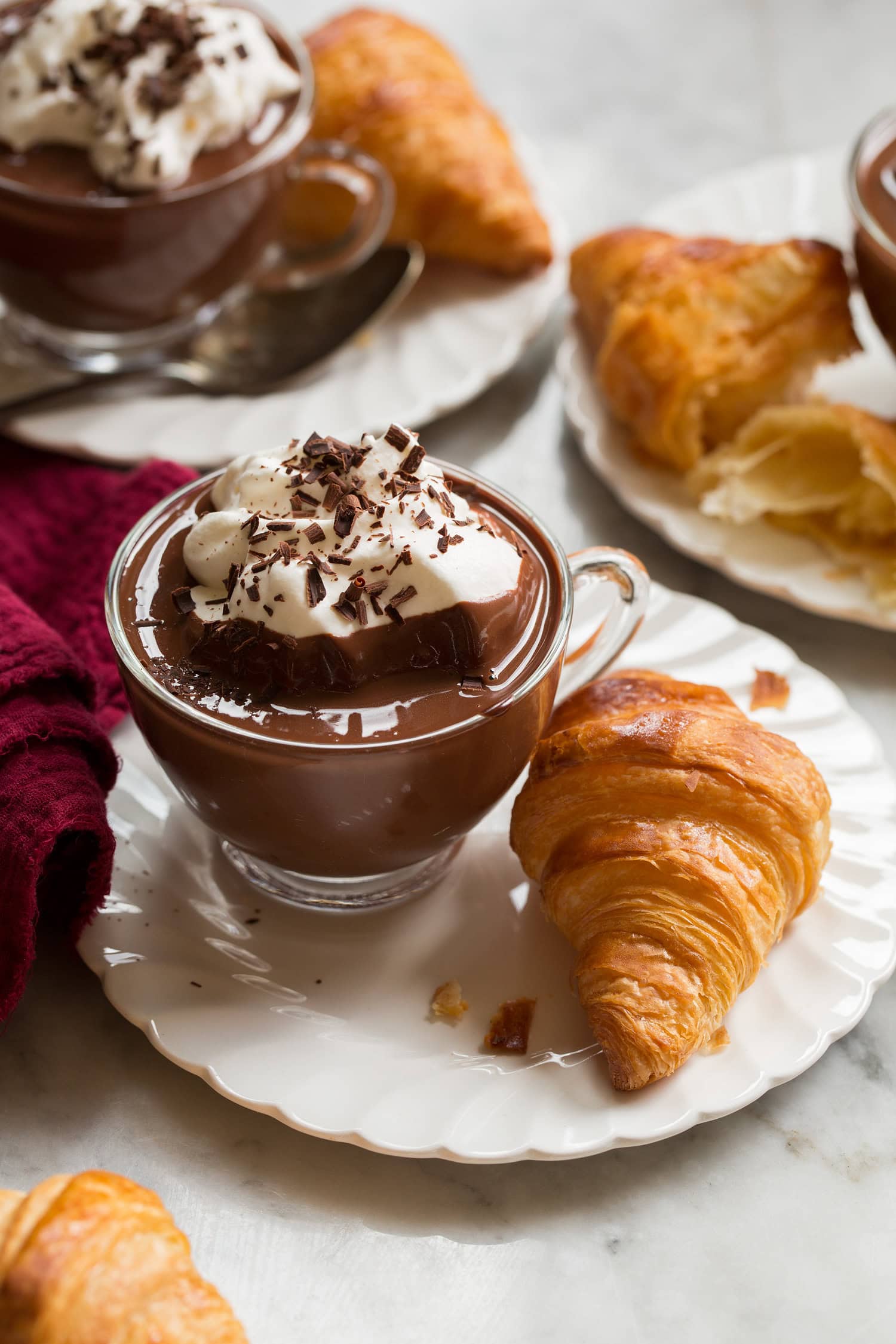 French Hot Chocolate French hot chocolate in a small glass mug served with a croissant on the side.