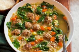 Italian wedding soup in a serving bowl with baguette bread and parmesan shown for serving.