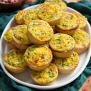 Mini quiche stacked on a white oval platter over a teal cloth.