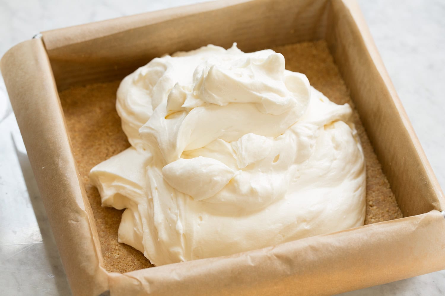 No Bake Cheesecake No bake cheese cake topping over graham cracker crust in pan before spreading.