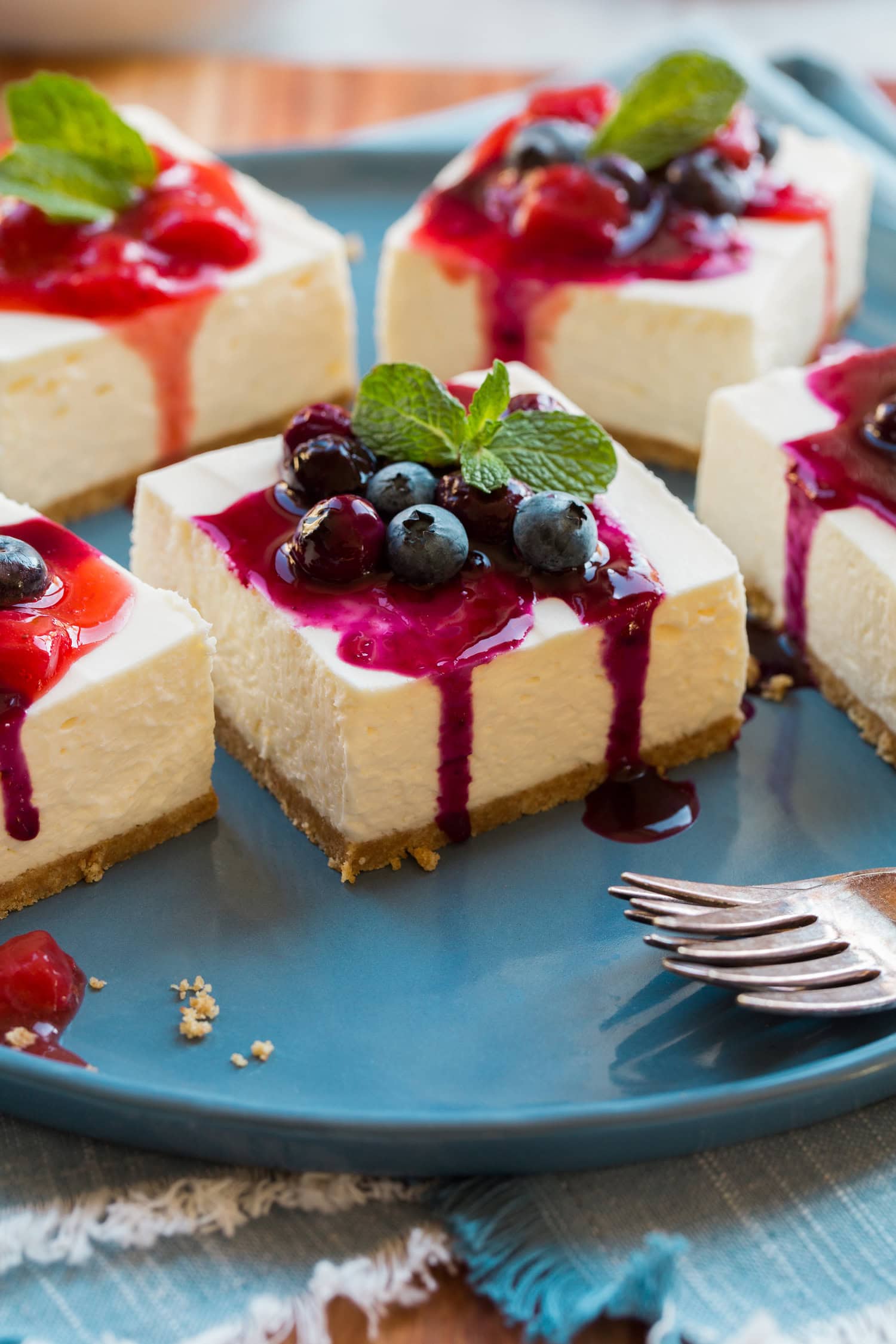 No Bake Cheesecake Bars No Bake Cheesecake bars shown with strawberry sauce and blueberry sauce, plus mint.