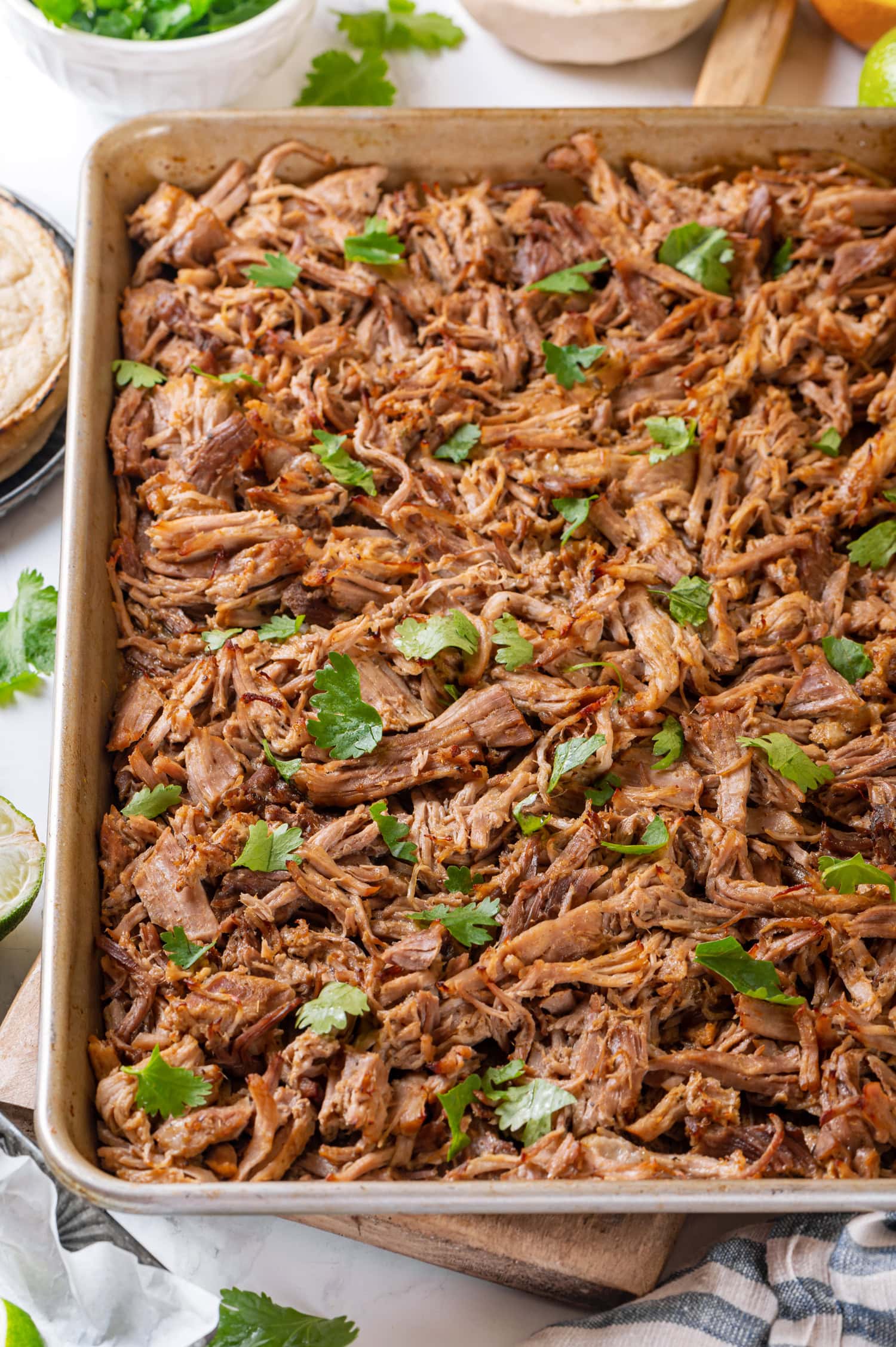 Shredded pork carnitas shown on a baking sheet after broiling.