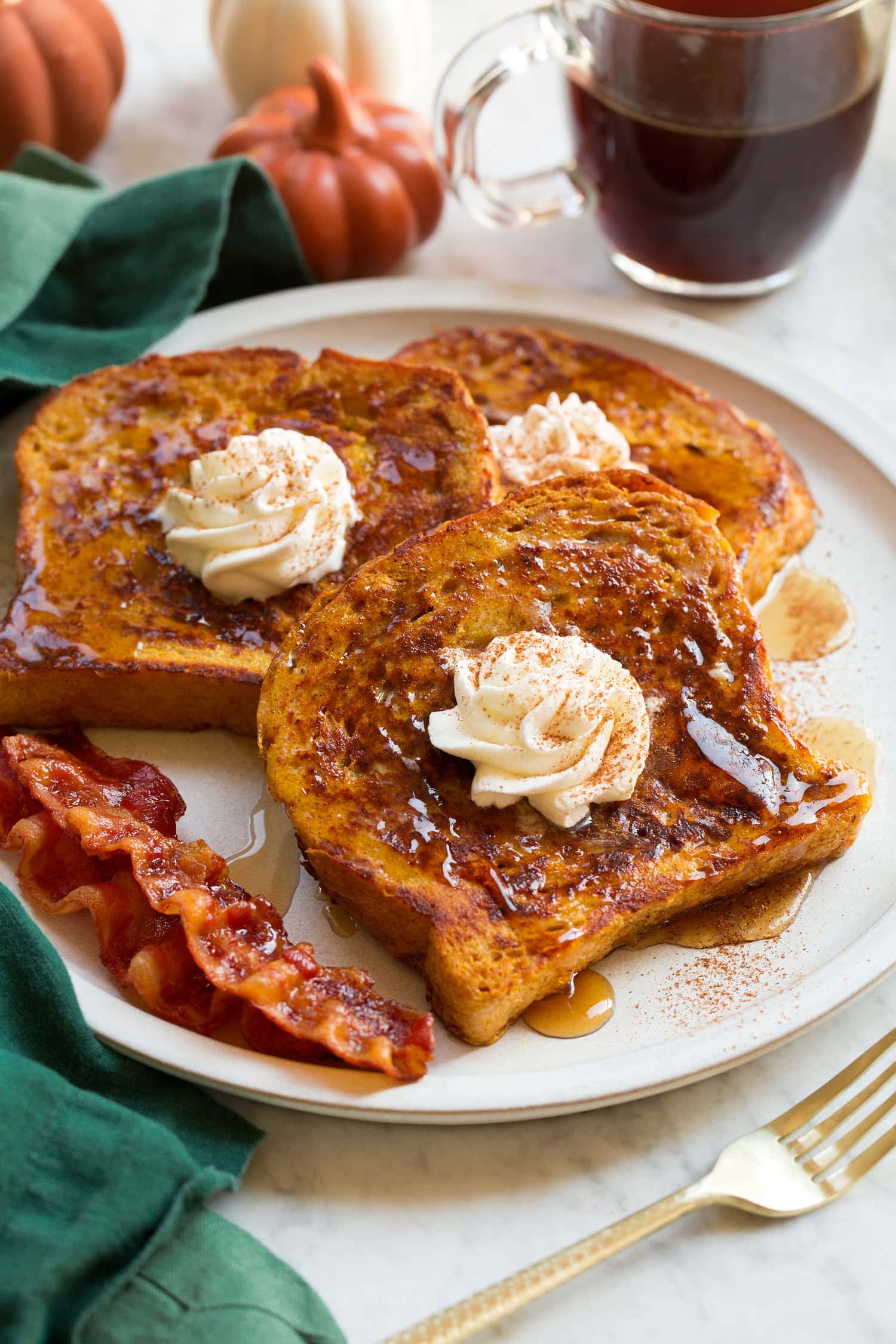 Three slices of homemade pumpkin french toast with maple syrup and whipped cream swirled on top.