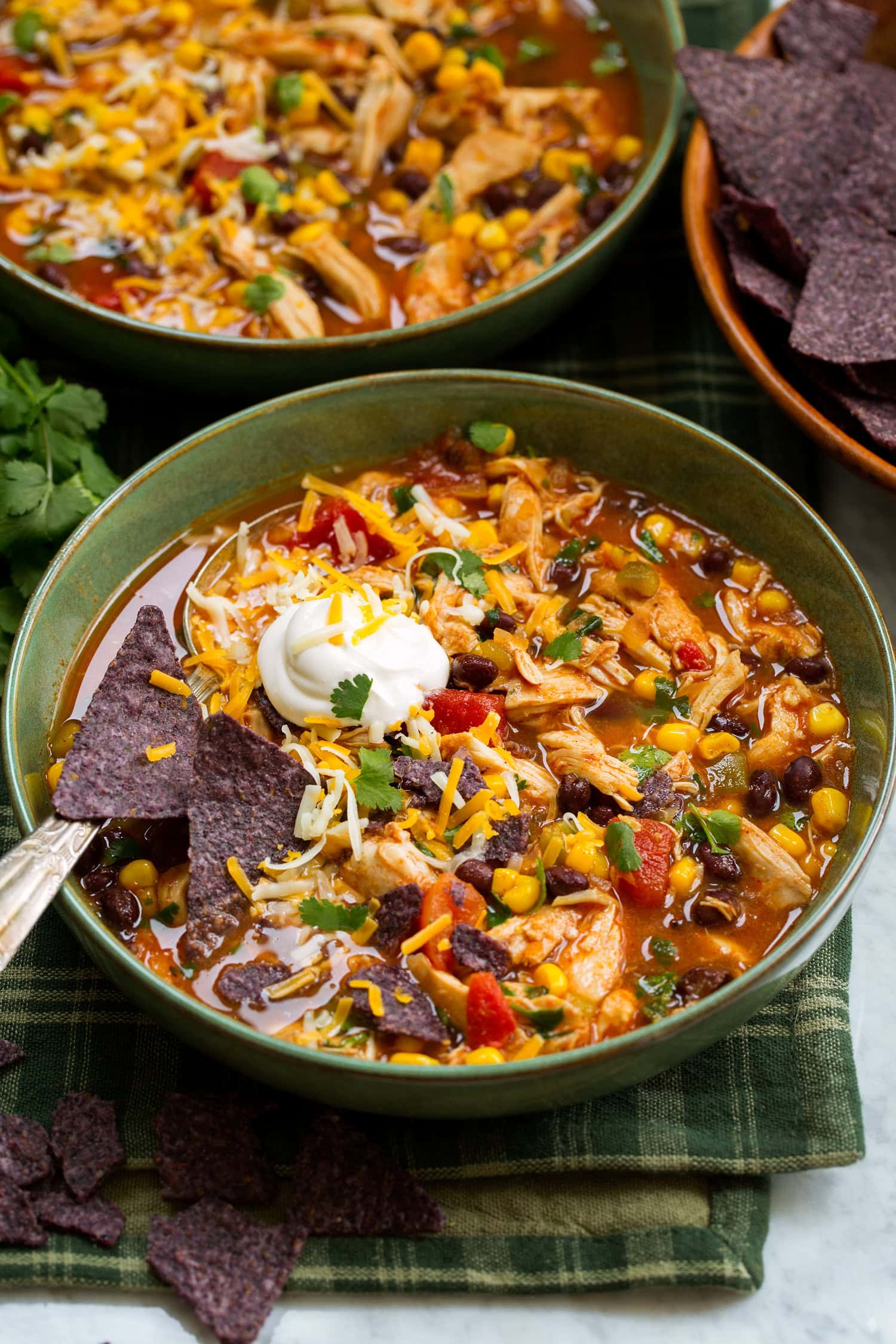 Green bowl filled with crockpot chicken tortilla soup, tortilla chips, sour cream and cilantro garnishes.