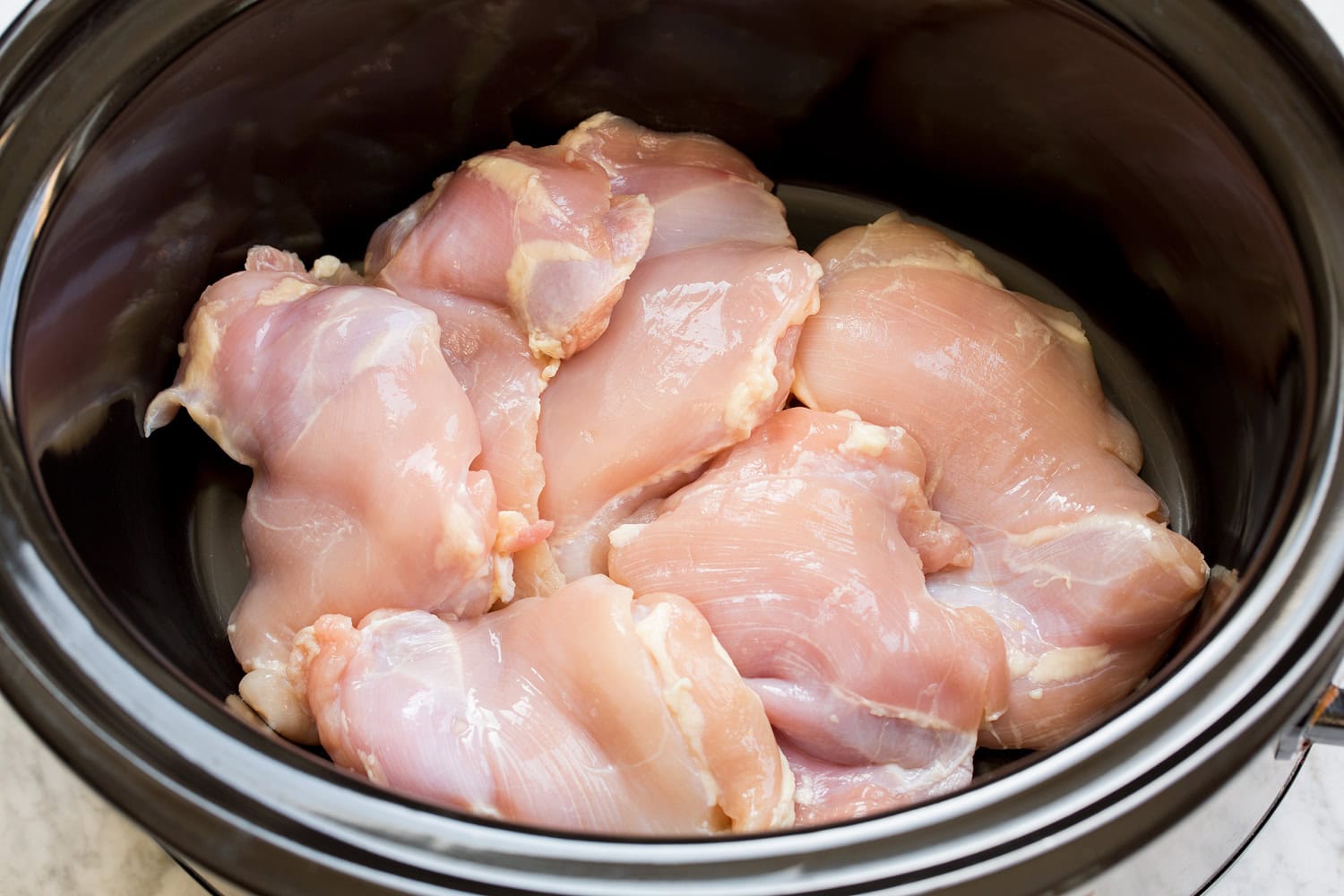 Raw chicken thighs in a crockpot insert.
