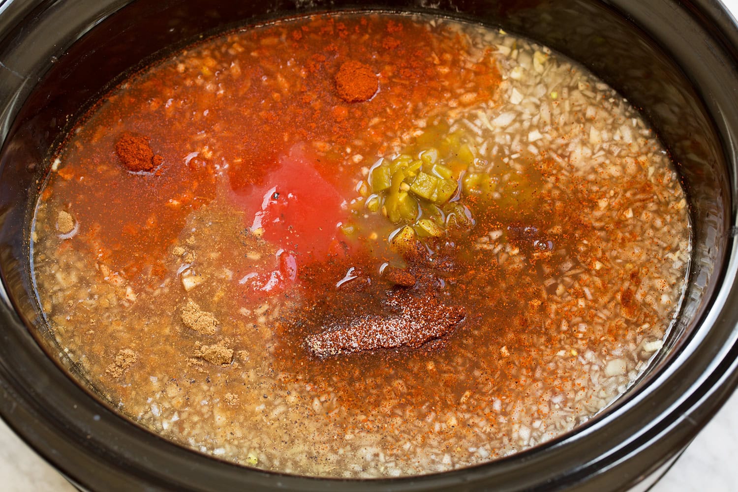 Broth, onions, seasonings, green chilies over chicken layer in slow cooker.