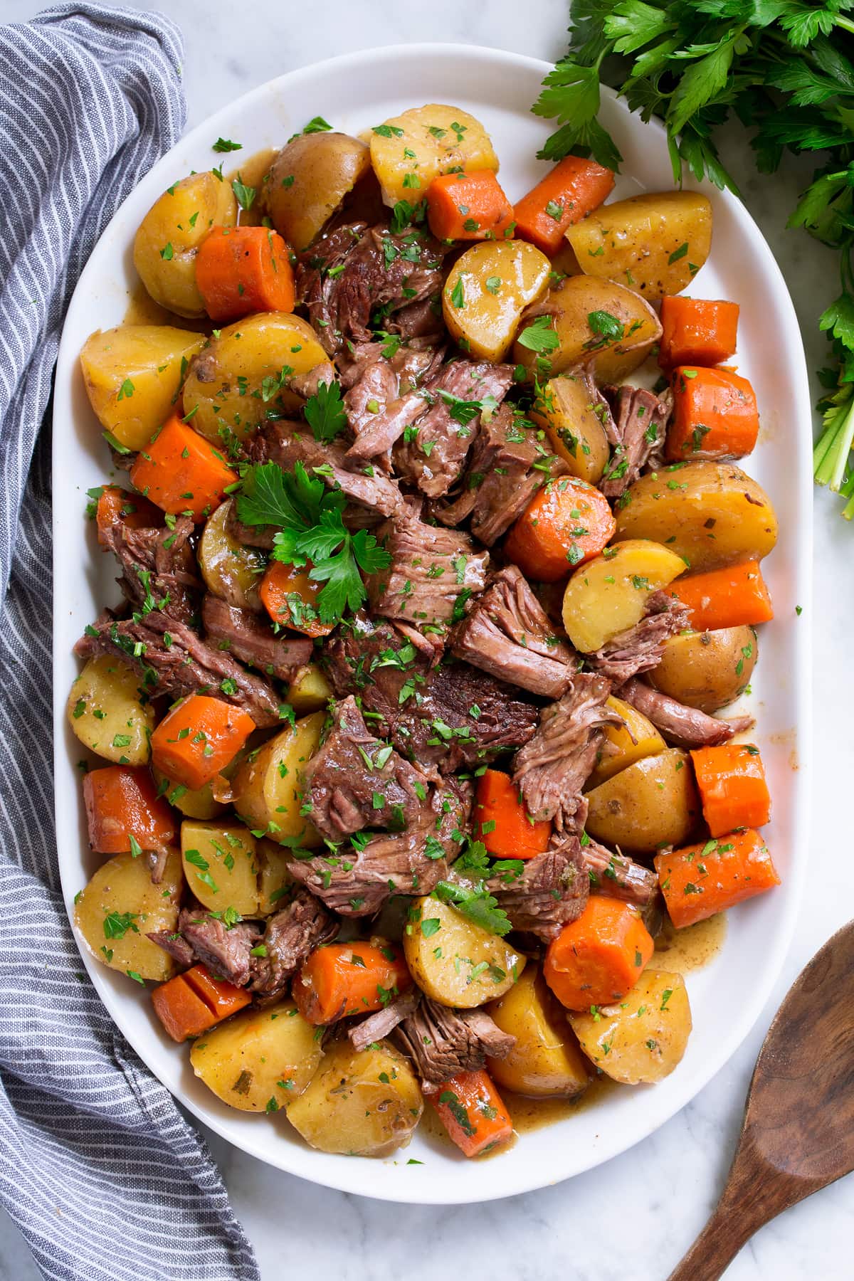 Best Ever Crockpot Roast! Slow Cooker Pot Roast with potatoes and carrots on a white oval serving platter set over marble.