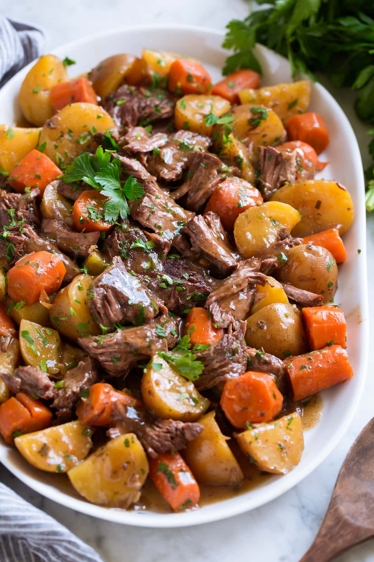 Best Ever Slow Cooker Pot Roast Shredded slow cooker pot roast with potatoes and carrots on a white serving platter garnished with parsley.
