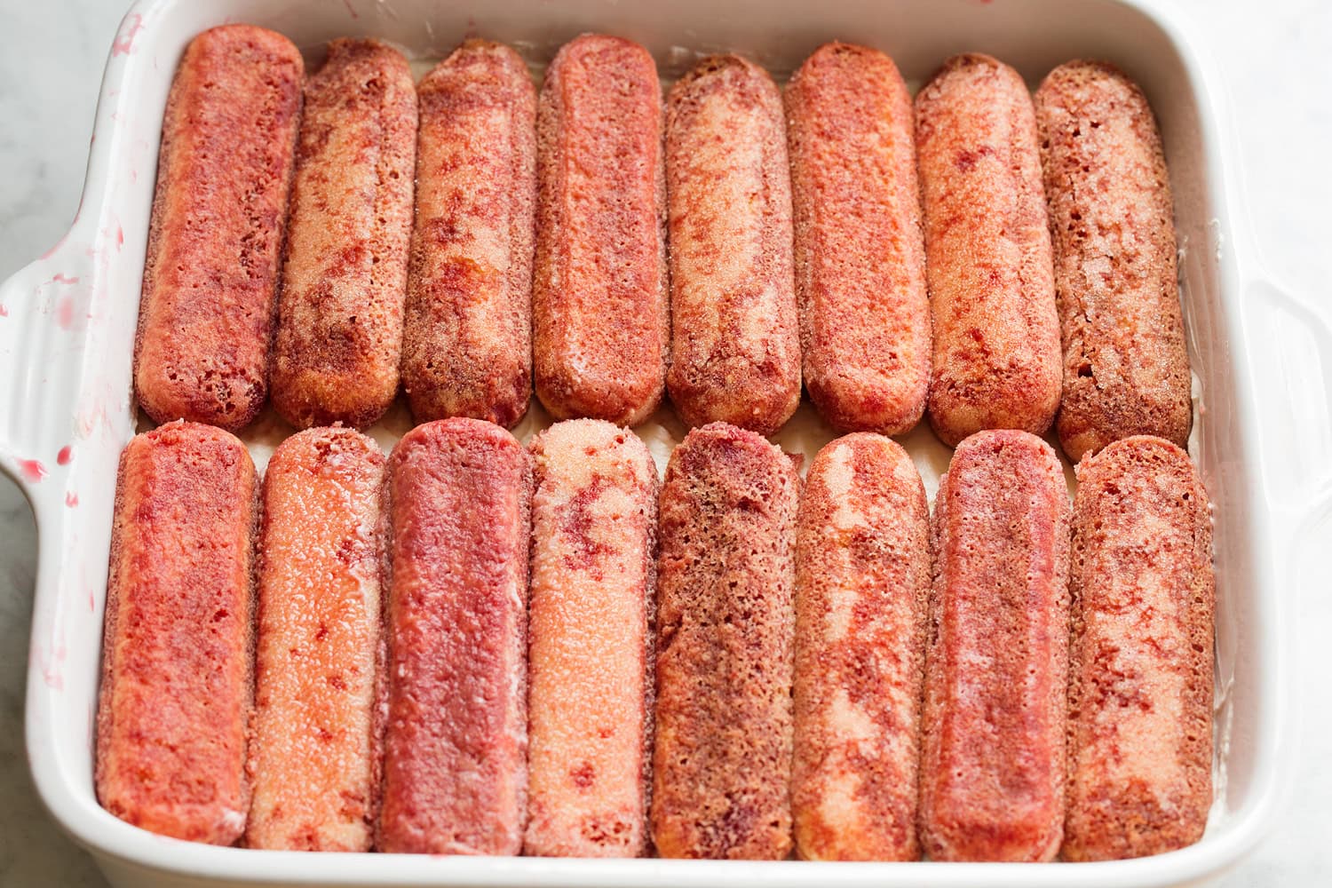 Juice soaked lady fingers in ceramic baking dish.