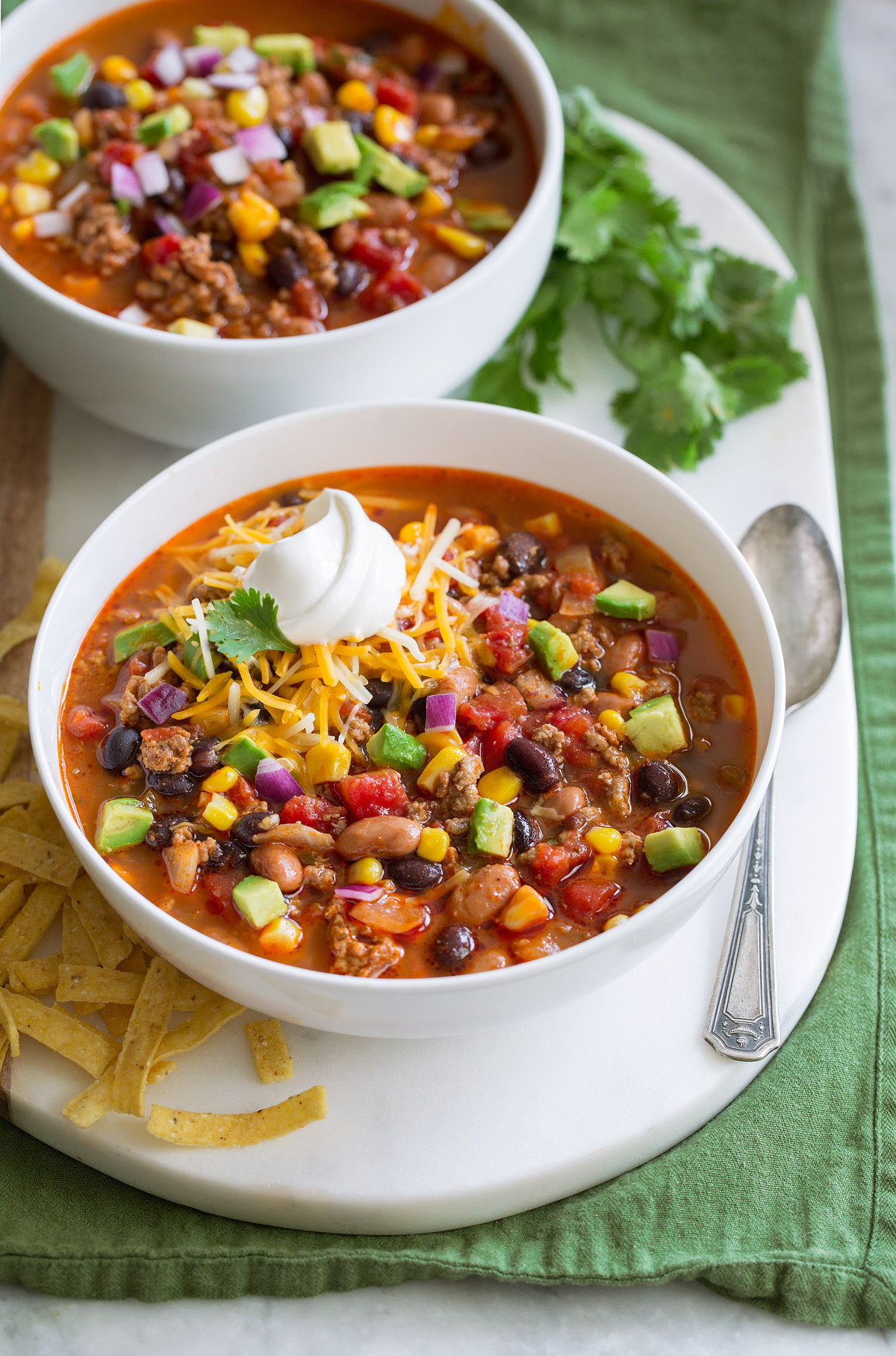 Taco Soup - easy, incredibly tasty soup! Loaded with hearty ingredients and brimming with delicious seasoned flavor. Perfect for cold fall and winter days! #tacosoup #soup #fall #recipe Two servings of taco soup in white bowls over a white platter.