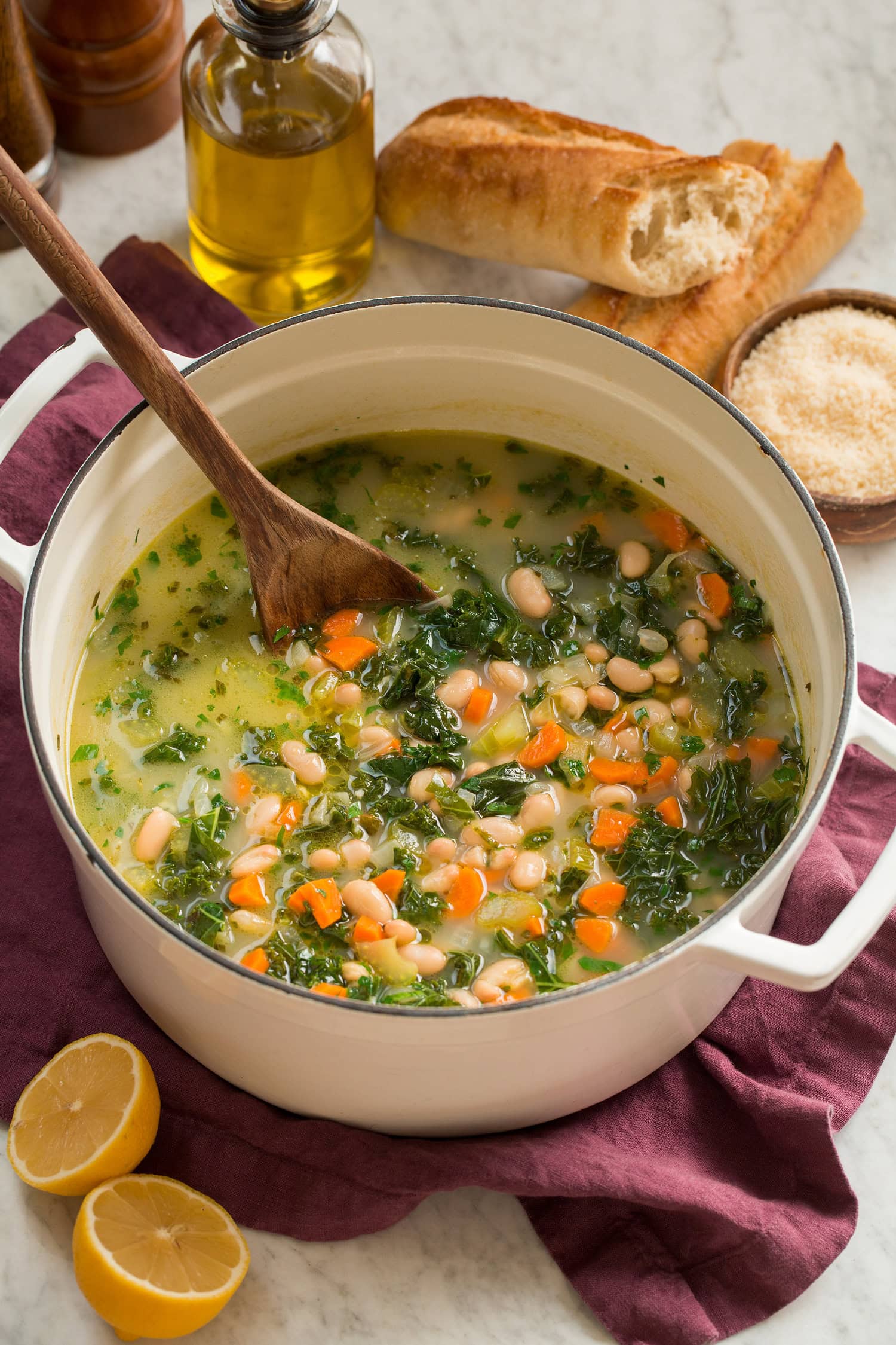 Pot of white bean kale soup with baguettes shown to the side for serving.